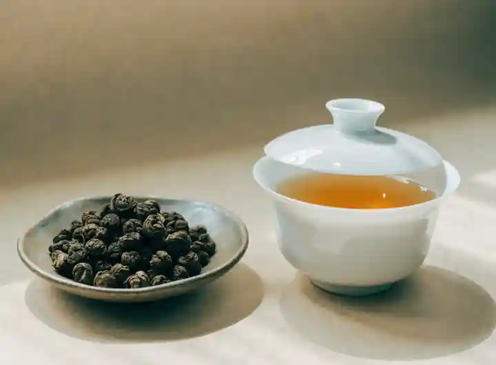 Zwinięte liście oolongu w ceramicznej miseczce obok porcelanowego gaiwanu